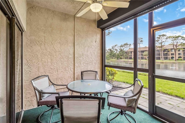 sunroom with ceiling fan and a water view