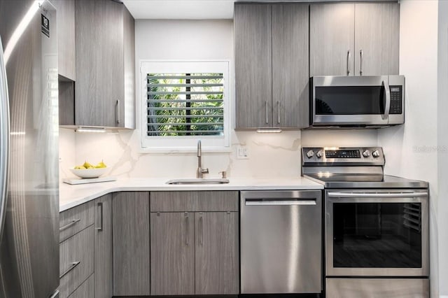 kitchen featuring gray cabinetry, stainless steel appliances, a sink, light countertops, and decorative backsplash