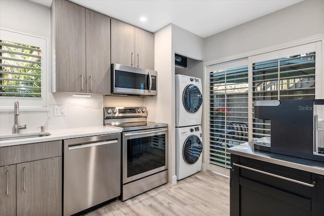 kitchen with stacked washer and clothes dryer, appliances with stainless steel finishes, light countertops, light wood-style floors, and a sink