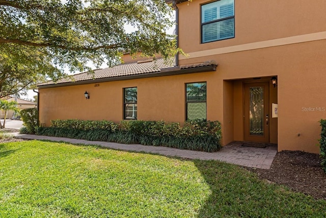 exterior space featuring a tile roof, a yard, and stucco siding