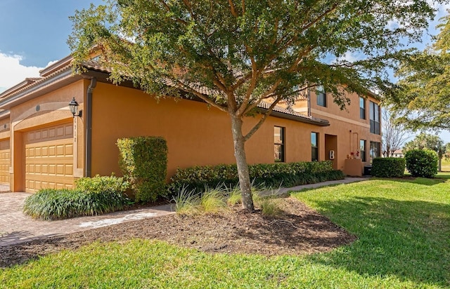 view of property exterior with an attached garage, a yard, a tiled roof, decorative driveway, and stucco siding