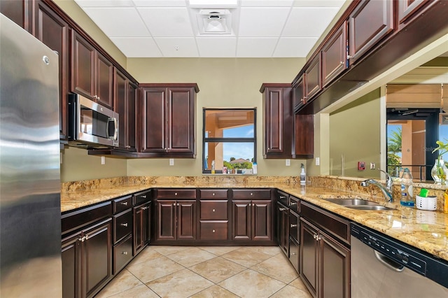 kitchen with a paneled ceiling, light stone counters, stainless steel appliances, and a sink