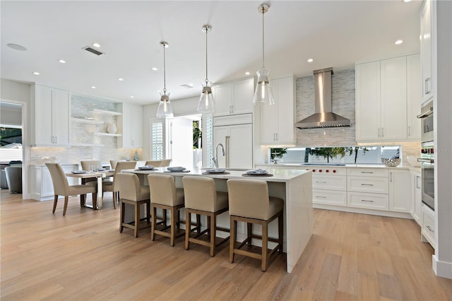 5103 Windward Ave, Sarasota, FL 34242 - kitchen featuring wall chimney exhaust hood, tasteful backsplash, paneled built in fridge, an island with sink, and light wood-style floors