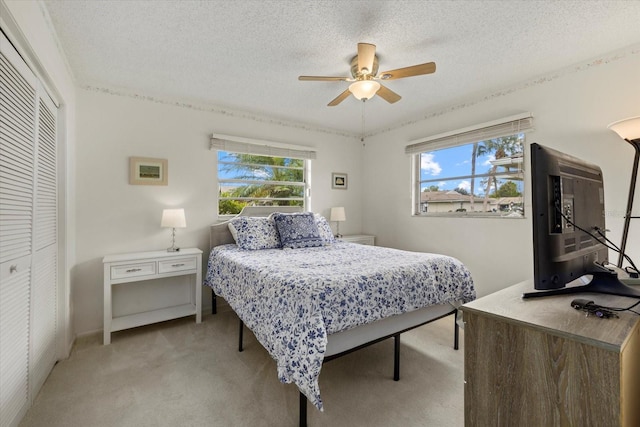 bedroom featuring light carpet, a closet, multiple windows, and a textured ceiling