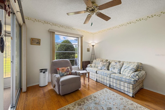 living area with a textured ceiling, wood finished floors, a ceiling fan, and baseboards