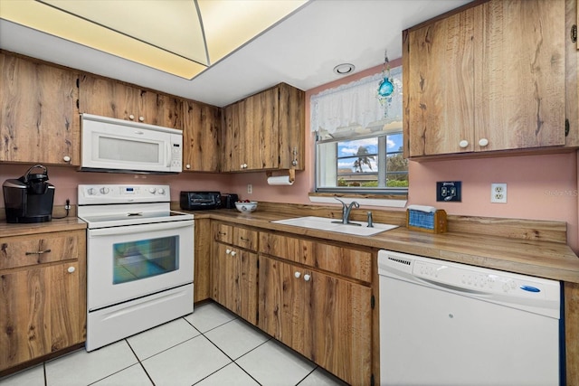 kitchen featuring brown cabinets, light tile patterned floors, light countertops, a sink, and white appliances