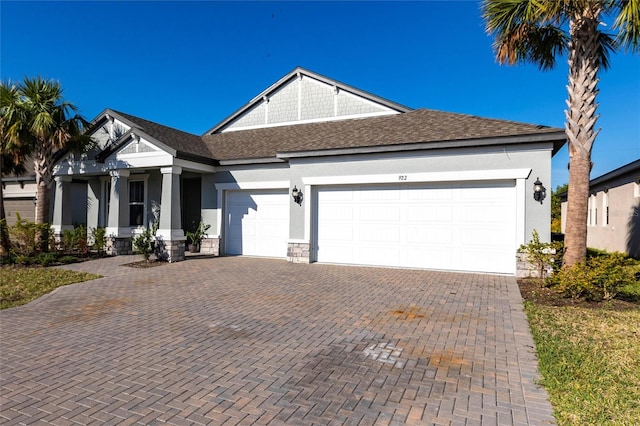 view of front facade featuring an attached garage, a shingled roof, stone siding, decorative driveway, and stucco siding