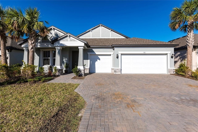 craftsman-style home with an attached garage, stone siding, decorative driveway, roof with shingles, and stucco siding