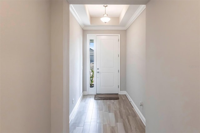 entryway with light wood-style floors, a raised ceiling, crown molding, and baseboards