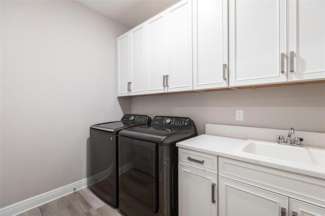 laundry room featuring washer and clothes dryer, cabinet space, light wood-style flooring, a sink, and baseboards