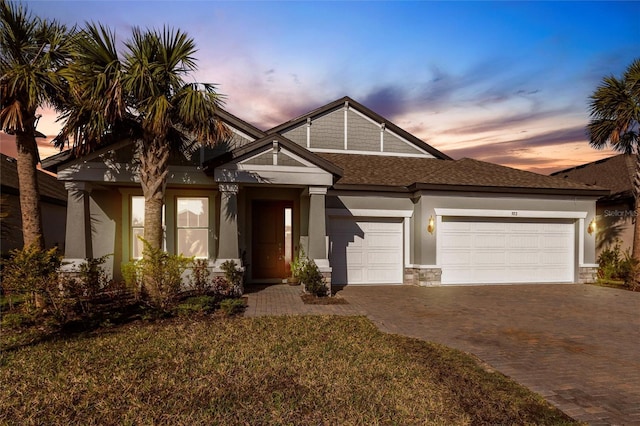 craftsman house featuring a garage, stone siding, decorative driveway, and stucco siding