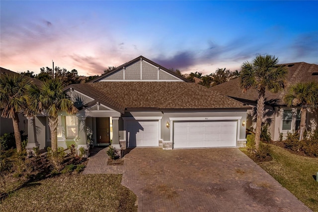 view of front of house with an attached garage, roof with shingles, decorative driveway, and stucco siding