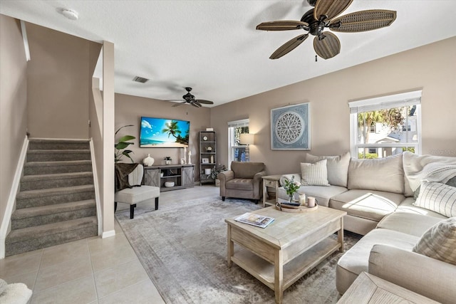 living room featuring light tile patterned floors, visible vents, a ceiling fan, stairway, and a textured ceiling