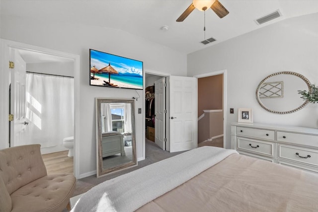 carpeted bedroom featuring lofted ceiling, ensuite bath, visible vents, and a walk in closet