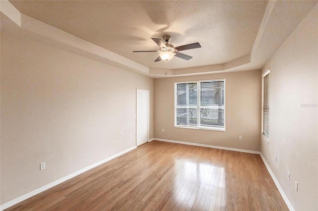 spare room with baseboards, ceiling fan, a tray ceiling, a textured ceiling, and light wood-type flooring