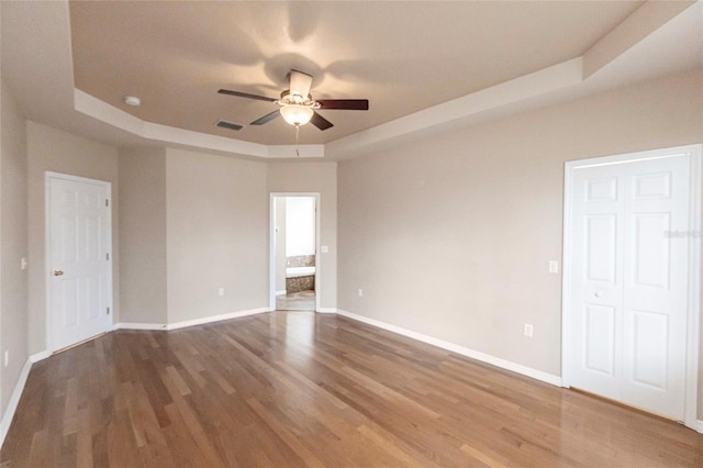 empty room featuring a ceiling fan, visible vents, a tray ceiling, and wood finished floors