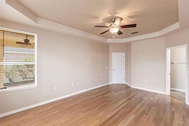 unfurnished bedroom featuring visible vents, baseboards, a raised ceiling, ceiling fan, and light wood-style flooring