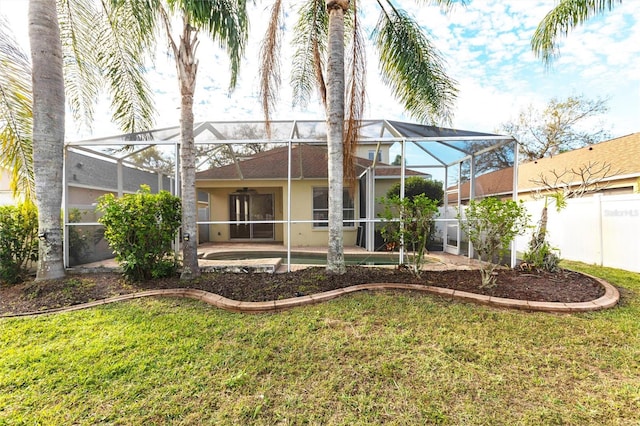 rear view of house featuring a yard, stucco siding, a patio area, fence, and a lanai