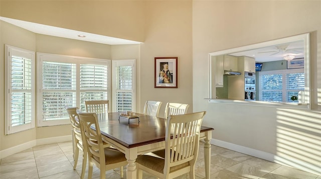 dining space featuring light tile patterned floors, ceiling fan, a high ceiling, and baseboards