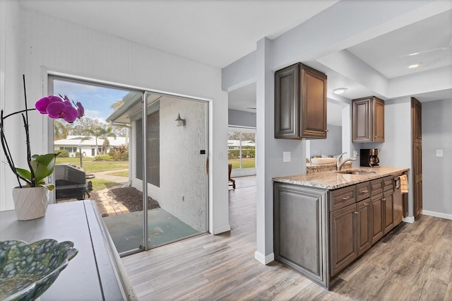 kitchen with light stone counters, light wood-type flooring, a sink, and baseboards