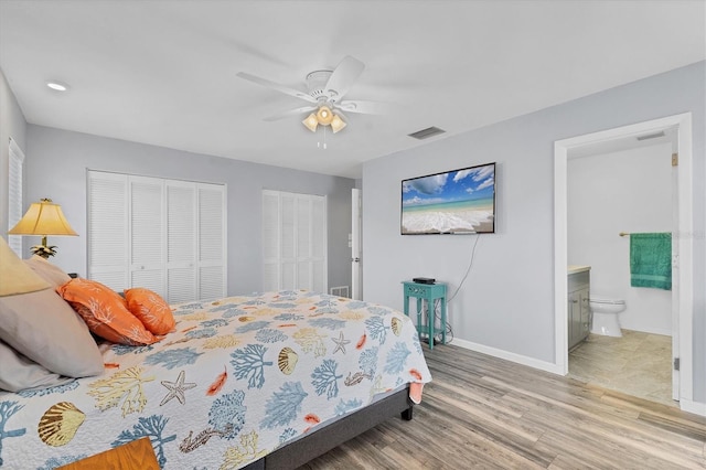 bedroom featuring visible vents, baseboards, ceiling fan, wood finished floors, and two closets