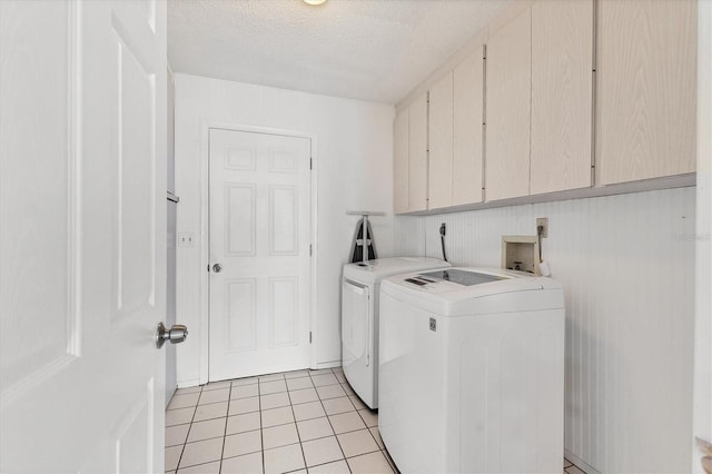 clothes washing area featuring washing machine and dryer, cabinet space, a textured ceiling, and light tile patterned flooring