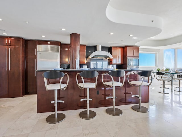 534 Beach Rd, Sarasota, FL 34242 - kitchen with dark countertops, wall chimney range hood, a breakfast bar area, and built in appliances