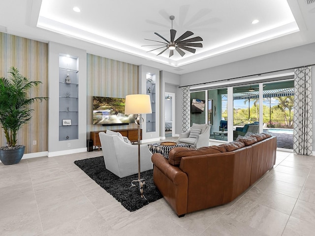 living area featuring built in shelves, a ceiling fan, baseboards, recessed lighting, and a raised ceiling