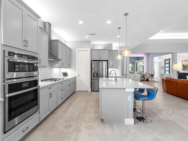 kitchen featuring open floor plan, gray cabinetry, stainless steel appliances, and wall chimney exhaust hood