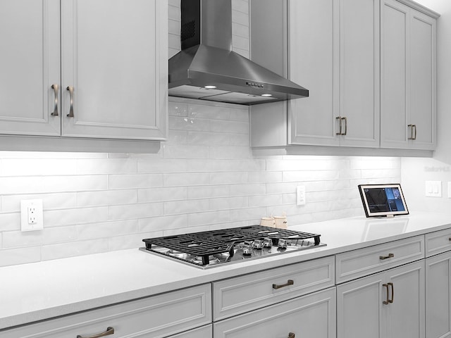 kitchen featuring light countertops, wall chimney range hood, tasteful backsplash, and stainless steel gas cooktop