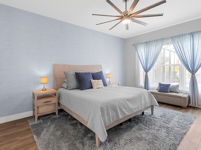 bedroom featuring ceiling fan, wallpapered walls, baseboards, and wood finished floors