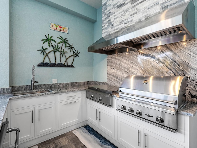 kitchen with decorative backsplash, white cabinets, wall chimney exhaust hood, and a sink