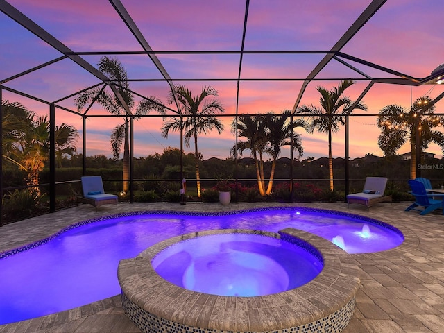 pool at dusk featuring glass enclosure, a patio, and a pool with connected hot tub