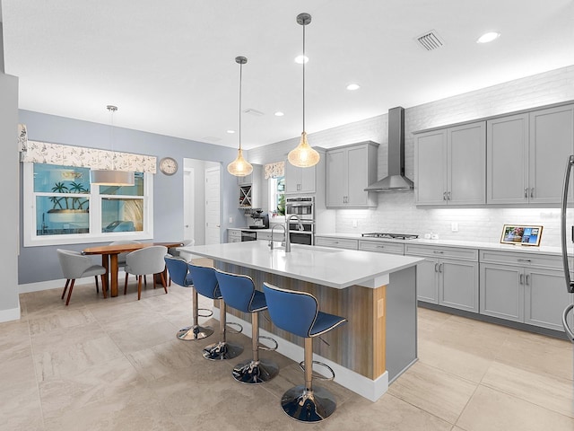 kitchen featuring visible vents, gray cabinetry, stainless steel appliances, and wall chimney exhaust hood