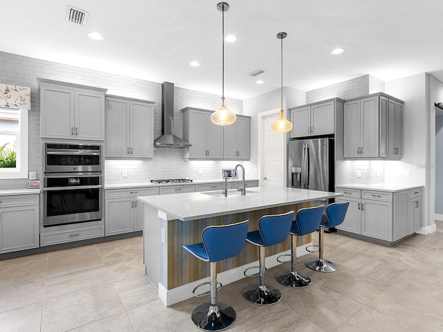 kitchen with visible vents, gray cabinets, stainless steel appliances, wall chimney exhaust hood, and a sink