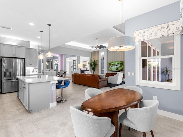 kitchen featuring stainless steel fridge with ice dispenser, a kitchen island with sink, gray cabinetry, a sink, and light countertops