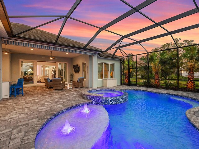 view of pool featuring a pool with connected hot tub, glass enclosure, an outdoor hangout area, ceiling fan, and a patio area