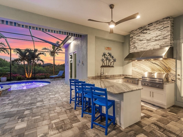 kitchen featuring wall chimney range hood, a breakfast bar area, a peninsula, white cabinets, and a sink