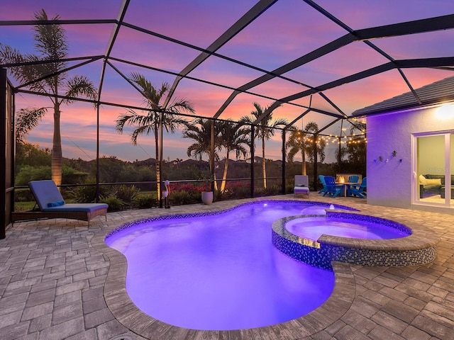 pool at dusk with glass enclosure, a patio area, and a pool with connected hot tub