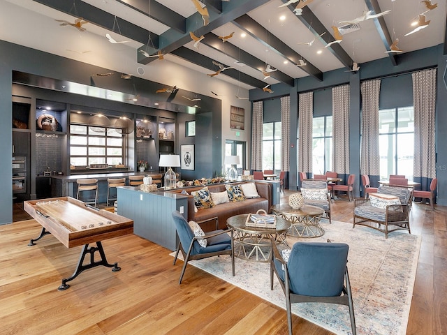 living area with visible vents, beamed ceiling, wood finished floors, and a towering ceiling