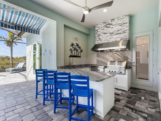 813 Tailwind Pl, Sarasota, FL 34240 - kitchen featuring wall chimney range hood, backsplash, a ceiling fan, dark stone counters, and white cabinetry