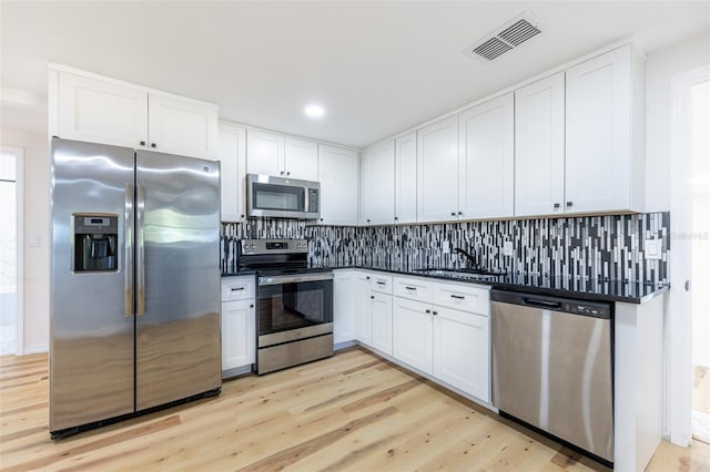 kitchen featuring dark countertops, visible vents, backsplash, stainless steel appliances, and a sink