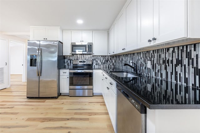 kitchen with tasteful backsplash, light wood finished floors, white cabinets, stainless steel appliances, and a sink