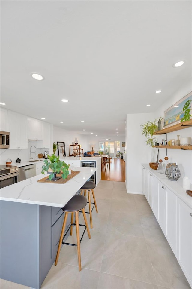 kitchen with light stone counters, stainless steel appliances, a breakfast bar, white cabinets, and a center island