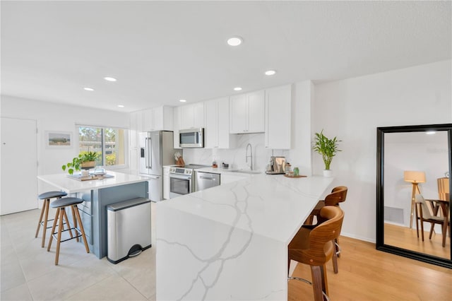 kitchen with a sink, stainless steel appliances, a kitchen bar, and white cabinets