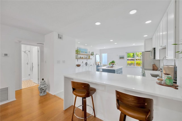 kitchen with a peninsula, light wood-type flooring, visible vents, and white cabinets