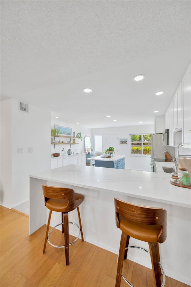 kitchen featuring light wood finished floors, light countertops, visible vents, white cabinets, and a peninsula