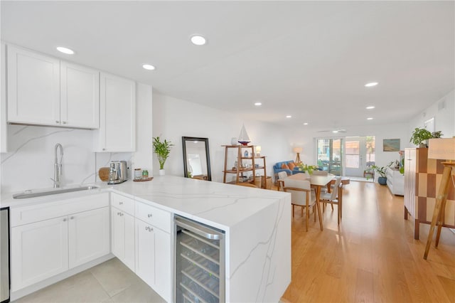 kitchen featuring light stone counters, wine cooler, open floor plan, a sink, and a peninsula