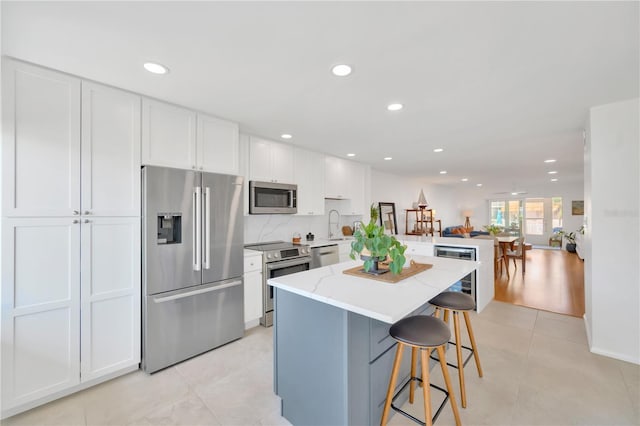 kitchen featuring light tile patterned floors, a kitchen island, a kitchen breakfast bar, stainless steel appliances, and white cabinetry