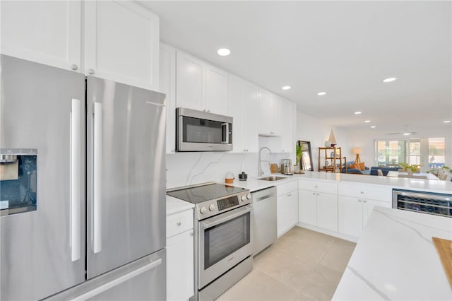 kitchen with light tile patterned floors, white cabinets, appliances with stainless steel finishes, a sink, and backsplash